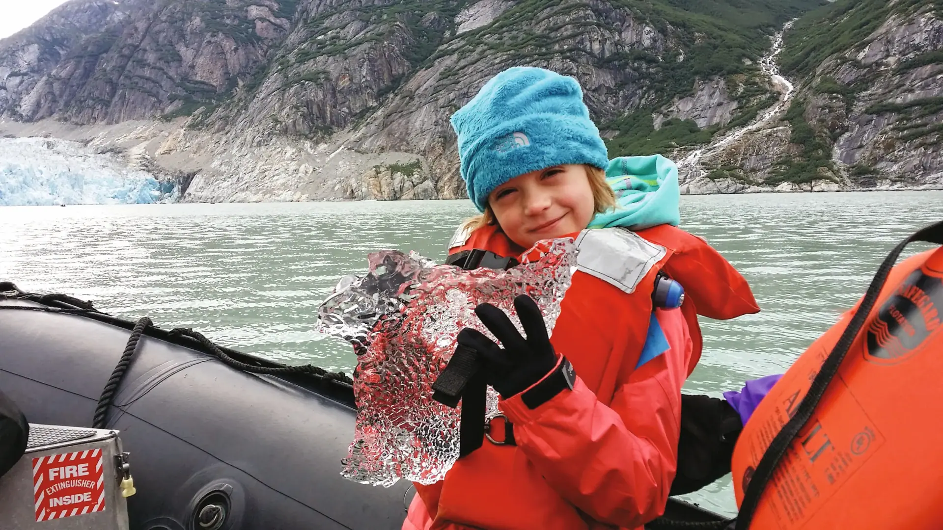 Child in a Zodiac holding glacier ice near a tidewater glacier in Alaska