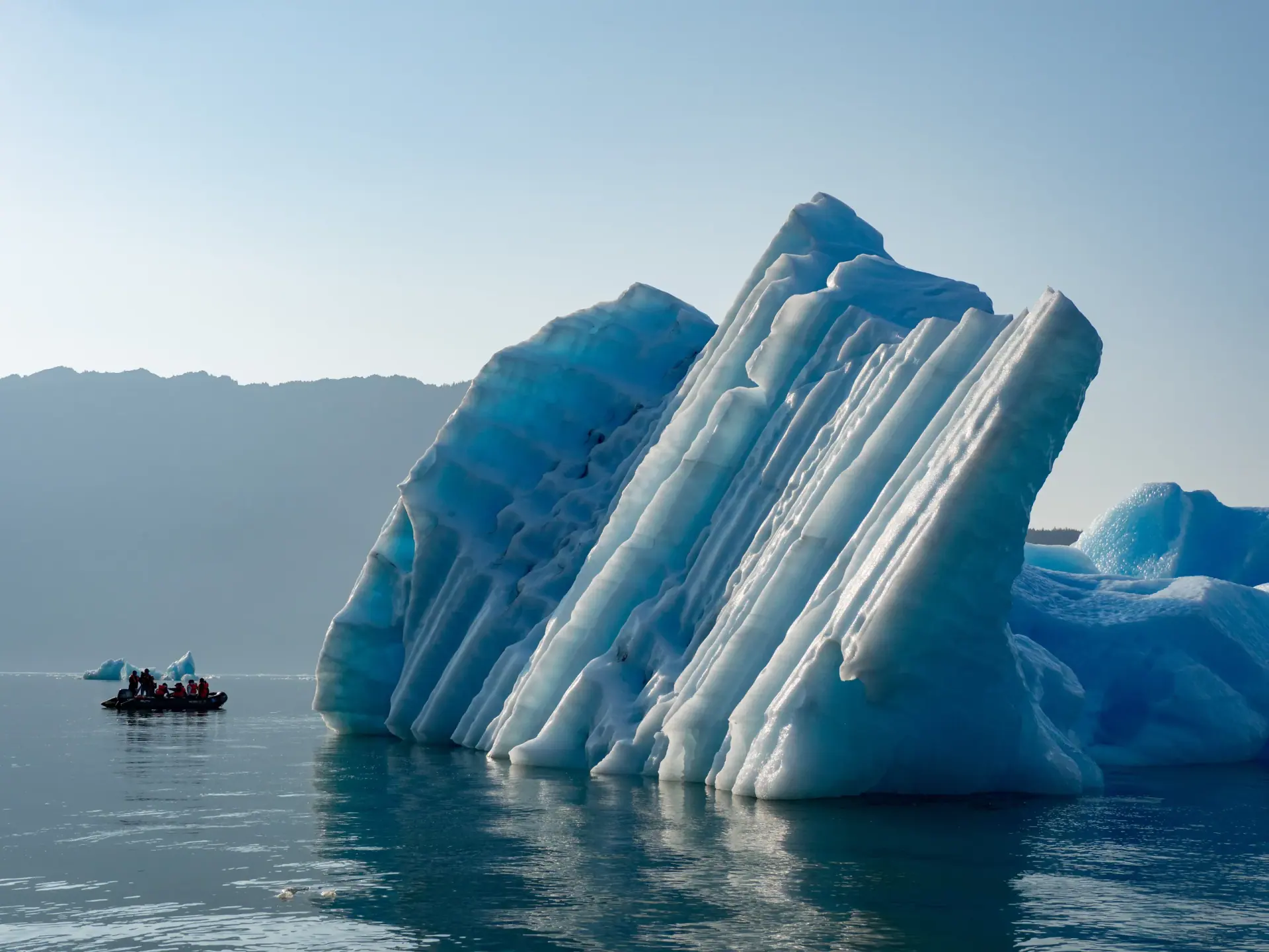 Expedition guests in a Zodiac beside a towering blue iceberg