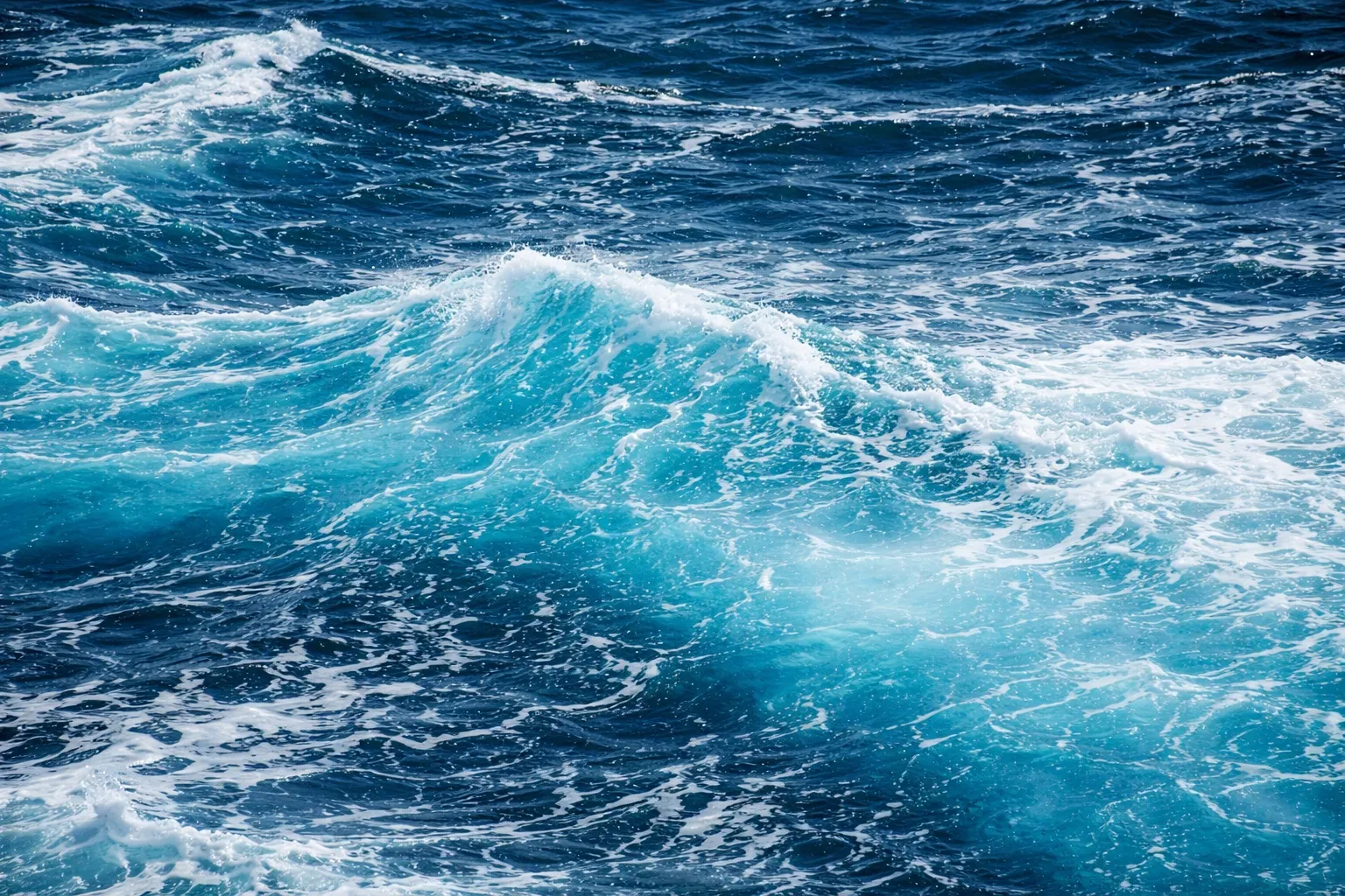 Crystal-clear turquoise ocean waves with white foam under natural daylight, showing dynamic sea movement
